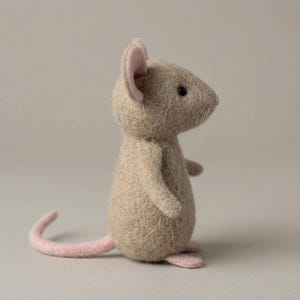 May include: A handmade felt mouse figurine in a standing pose. The mouse has a light tan body, pink ears, a pink tail, and pink feet. It has small black eyes and white whiskers. The figurine is a charming decorative item.
