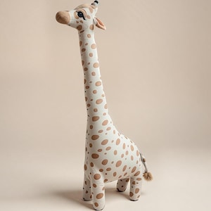 Puede incluir: Un juguete de peluche con forma de jirafa de pie. La jirafa tiene un cuello largo y está cubierta de manchas marrones sobre un fondo crema. La cara, las orejas y las pezuñas son marrones. La cola tiene un pequeño mechón marrón.