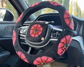 May include: Black crochet steering wheel cover and center console cover with a repeating pink and red floral design. The covers are handmade and add a decorative touch to a car's interior.