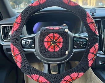 May include: Black and red crocheted steering wheel cover and matching center console cover. The steering wheel cover has a repeating pattern of red flower-like shapes. The center console cover has a single red flower design.