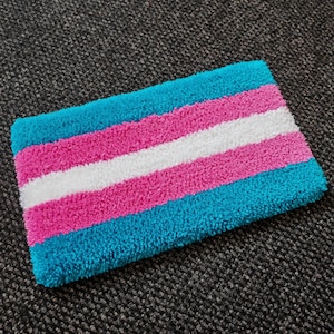 May include: A rectangular tufted rug featuring horizontal stripes in a repeating pattern of light blue, pink, and white. The textile has a thick, plush, and textured pile surface with clean, straight edges and a consistent, dense fibre construction.