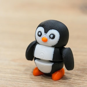 May include: A 3D-printed penguin figurine. The penguin has a black head and wings, a white belly, and orange feet and beak. The penguin's eyes are white with black pupils. The figurine is made of plastic and has a textured surface.