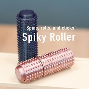 May include: Two spiky rollers are shown, one dark blue and one copper-coloured. The copper roller is in focus, displaying its textured surface and cylindrical shape. The text "Spins, rolls, and clicks! Spiky Roller" is overlaid on the image.