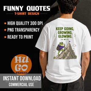 May include: A white t-shirt featuring a graphic on the back of a green frog wearing a purple hoodie and a backpack, climbing a grey mountain with a flag at the peak. The text above the frog reads, KEEP GOING, GROWING, GLOWING, in green letters.