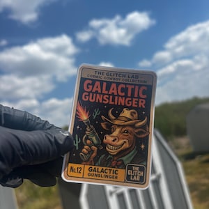 May include: A rectangular sticker from The Glitch Lab's Cosmic Cowboy Collection. The sticker features a cartoon cow wearing a cowboy hat and holding a ray gun. The text "GALACTIC GUNSLINGER" is prominently displayed.