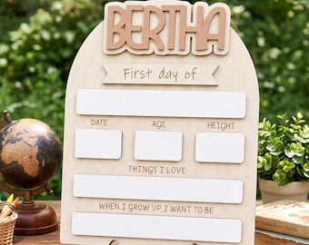 Peut inclure: Un panneau en bois en forme d'arche avec le nom BERTHA en haut, comportant des espaces blancs pour noter la date, l'âge, la taille, les choses aimées et le métier souhaité, soutenu par un support en bois sur une surface plane.