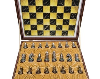 Juego de ajedrez de metal ornamentado, con detalles de esmeraldas y rubíes, piezas de ajedrez lastradas y caja forrada de terciopelo.