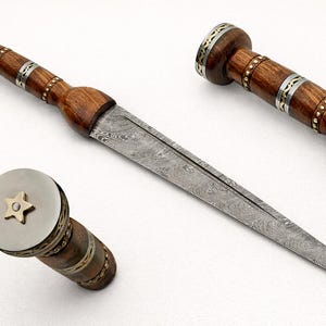 May include: A detailed image of a dagger with a wooden handle and a patterned steel blade. The handle is brown with silver and gold accents. The blade has a unique, textured pattern. The dagger is displayed on a white background.