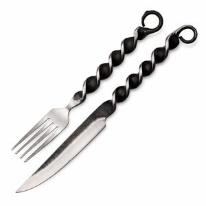 May include: A forged metal fork and knife set. The handles have a twisted design, and the knife has a sharp, pointed blade. The fork has three tines. The set is designed for outdoor cooking or dining.
