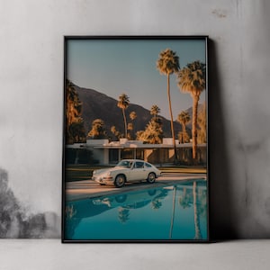 Könnte beinhalten: Gerahmter Druck mit einem klassischen weißen Sportwagen an einem türkisfarbenen Pool. Im Hintergrund sind Palmen, ein Haus im Stil der Moderne, Berge und ein klarer blauer Himmel zu sehen.
