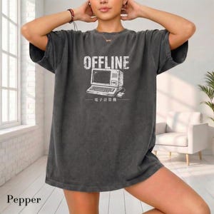 Może przedstawiać: Ciemnoszary t-shirt oversize z białym nadrukiem graficznym przedstawiającym komputer w stylu vintage, napisem OFFLINE powyżej oraz japońskimi znakami poniżej. Koszulka ma okrągły dekolt, krótkie rękawy i wykończenie materiału o spranym wyglądzie.
