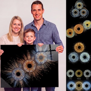 May include: A family presents a framed print with detailed close-ups of human irises. The artwork displays three eyes with intricate patterns in shades of blue, brown, and gold, set against a black background. Additional iris variations are shown on the right.