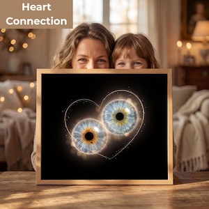 Op de afbeelding: Een ingelijste print met twee gedetailleerde oogillustraties, één bruin en één blauw, tegen een zwarte achtergrond. De ogen zijn verbonden door een gouden hartomtrek, met de woorden "Heart Connection" bovenaan.
