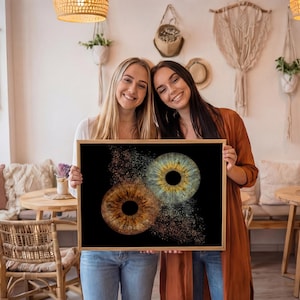 May include: A rectangular framed print featuring a high-resolution graphic of two human irises against a solid black background. One iris is brown with gold flecks, and the other is blue-green with gold details, both appearing to dissolve into particles.