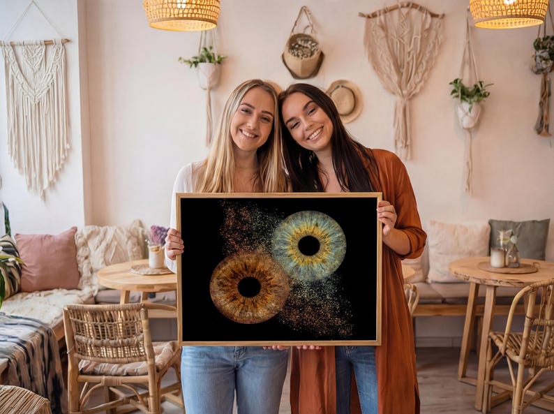 May include: A rectangular framed print featuring a high-resolution graphic of two human irises against a solid black background. One iris is brown with gold flecks, and the other is blue-green with gold details, both appearing to dissolve into particles.