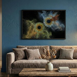 May include: A rectangular wall art print in a black frame featuring two human irises centered against a black background, surrounded by swirling clouds of gold and blue dust particles that create a vibrant, explosive visual effect.
