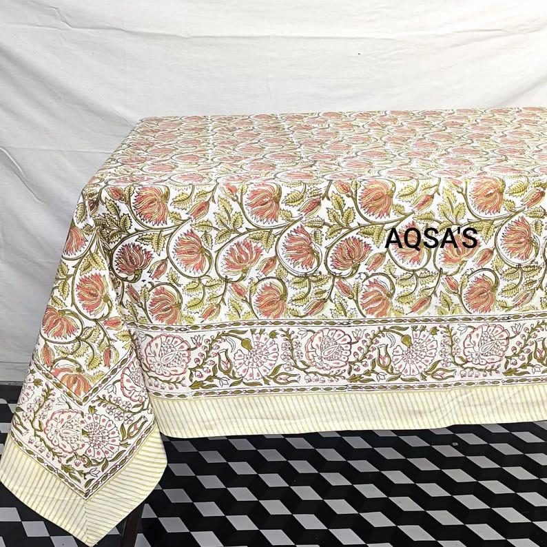 K&ouml;nnte beinhalten: Blumen-Tischdecke mit einem sich wiederholenden Muster aus rosa Bl&uuml;ten und gr&uuml;nen Bl&auml;ttern auf wei&szlig;em Hintergrund. Der Rand hat ein detailliertes Blumendesign. Der Text "AQSA'S" ist auf der Tischdecke zu sehen.