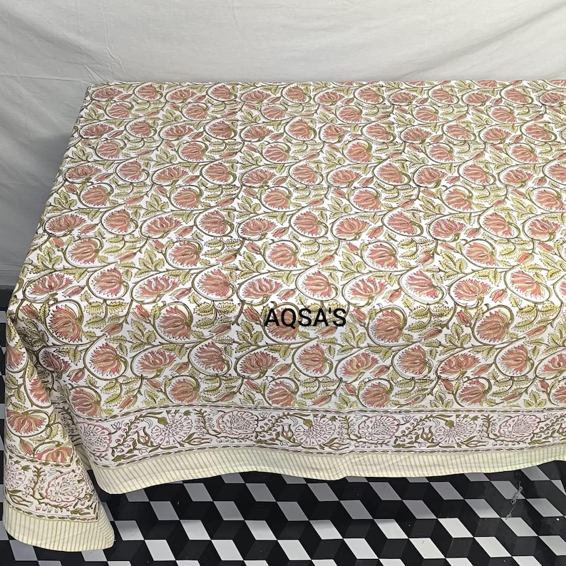K&ouml;nnte beinhalten: Eine Steppdecke mit floralem Muster mit wei&szlig;em Hintergrund und rosa und gr&uuml;nen Blumen. Die Steppdecke hat einen Rand mit einem &auml;hnlichen floralen Design. Der Text "AQSA'S" ist auf die Steppdecke gedruckt.