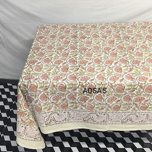 K&ouml;nnte beinhalten: Eine Steppdecke mit floralem Muster mit wei&szlig;em Hintergrund und rosa und gr&uuml;nen Blumen. Die Steppdecke hat einen cremefarbenen Rand und der Text "AQSA'S" ist sichtbar. Die Steppdecke wird wahrscheinlich f&uuml;r Bettw&auml;sche oder als dekorativer &Uuml;berwurf verwendet.