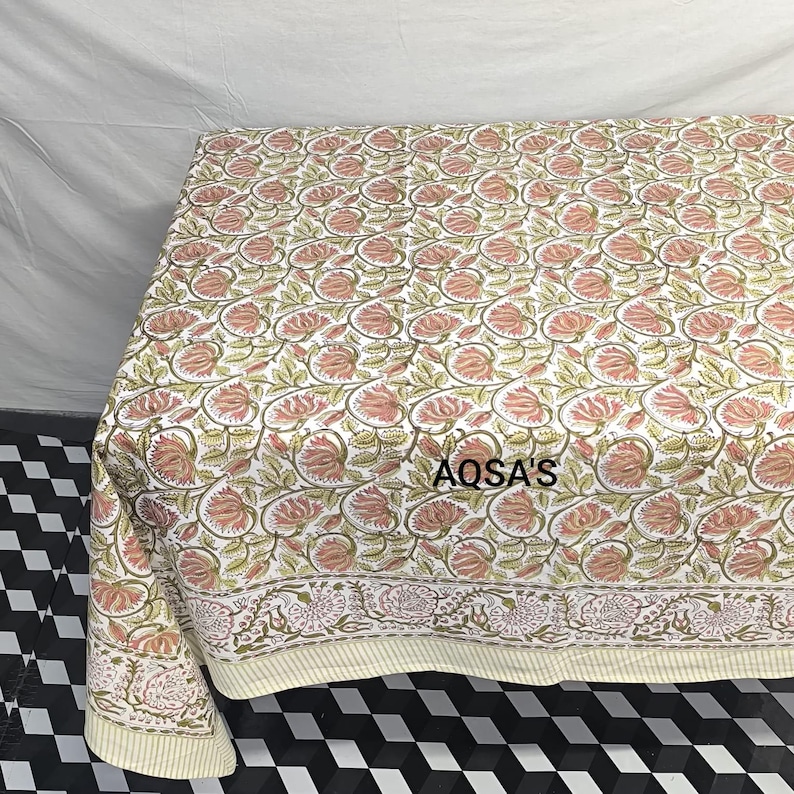 K&ouml;nnte beinhalten: Eine Steppdecke mit floralem Muster mit wei&szlig;em Hintergrund und rosa und gr&uuml;nen Blumen. Die Steppdecke hat einen cremefarbenen Rand und der Text "AQSA'S" ist sichtbar. Die Steppdecke wird wahrscheinlich f&uuml;r Bettw&auml;sche oder als dekorativer &Uuml;berwurf verwendet.