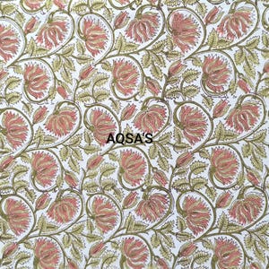 K&ouml;nnte beinhalten: Wei&szlig;er Stoff mit einem sich wiederholenden Blumenmuster. Die Bl&uuml;ten sind zartrosa mit gelben Zentren, die Bl&auml;tter olivgr&uuml;n. Der Text "AQSA'S" ist in Schwarz gedruckt. Das Design ist im Blockdruckstil gehalten.