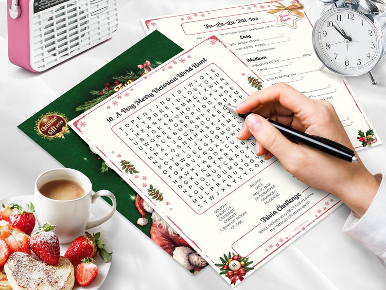 Peut inclure: Image sur le th&egrave;me de No&euml;l avec des jeux de mots et des &eacute;nigmes &agrave; compl&eacute;ter, une tasse de caf&eacute; et des fraises. Une main tient un stylo pour compl&eacute;ter les &eacute;nigmes. Une radio rose et un r&eacute;veil argent&eacute; sont &eacute;galement visibles.