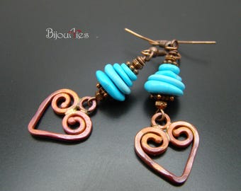 May include: A pair of handcrafted earrings featuring copper heart-shaped pendants with spiral details. The earrings have turquoise blue beads and copper accents. The word "Bijoueries" is printed on the top left.