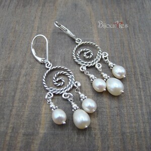 May include: Silver-toned dangle earrings with a spiral design and three dangling white pearls. The earrings have a lever-back closure. The word "Bijouteries" is written in cursive on the top right.