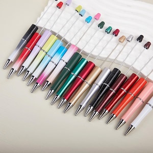 May include: A selection of colourful pens with silver detailing. The pens display a range of colours, such as red, pink, green, and blue, with a silver tip and a small, decorative top. The pens are arranged in a diagonal row.