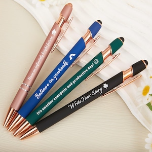 May include: A selection of pens in shades of rose gold, blue, green, and black. Each pen has a metallic finish and features motivational text like "Believe in yourself." The pens have a stylish design with a clip and measure approximately 14 cm in length.