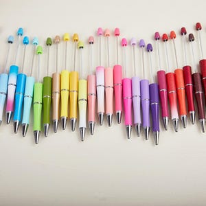 May include: A collection of colorful pens with silver tips and slender, curved barrels. The pens come in a variety of colors, including blue, green, yellow, pink, purple, red, and black. Each pen has a small, decorative top.