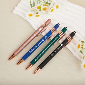 May include: Four pens with rose gold detailing. The pens are in pink, blue, green, and black. Each pen has an inspirational message: "Have an infinitely bright future", "Believe in yourself", "It's another energetic and productive day!", and "Write Your Story".