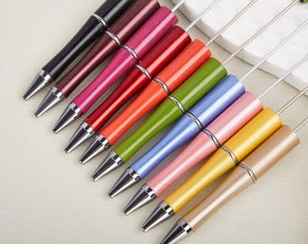 May include: A collection of colorful pens with silver accents. The pens feature a variety of colors, including black, burgundy, pink, red, orange, green, blue, and gold. Each pen has a silver tip and a matching colored top.