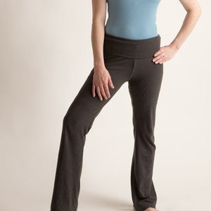 May include: A woman wearing a light blue tank top and dark grey yoga pants. She is standing with her weight on one leg and her other leg slightly bent.