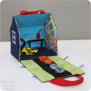 Peut inclure: Une maison de jeu en denim bleu et en tissu avec une poign&eacute;e rouge, ouverte pour r&eacute;v&eacute;ler une route verte et noire avec trois voitures miniatures. L'int&eacute;rieur de la maison de jeu est d&eacute;cor&eacute; d'un tissu bleu et blanc avec des panneaux de signalisation.
