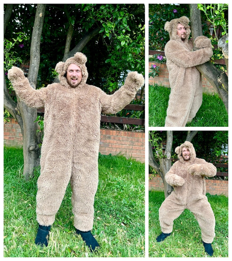 May include: A person wearing a brown furry bear costume with a hood. The person is standing in a grassy area with trees in the background.