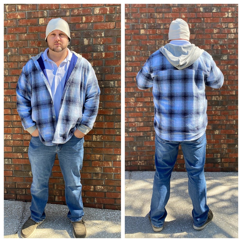 May include: A blue and black plaid flannel shirt with a gray hooded liner. The shirt is worn over a white collared shirt. The person is wearing a white beanie.