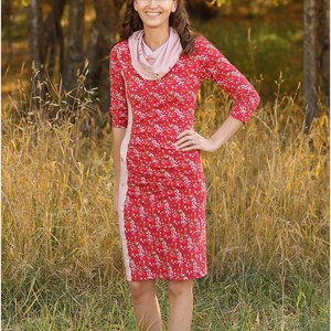 May include: A woman wearing a red floral dress with a white and red striped scarf. The dress has a side panel of white and red stripes. She is standing in a field of tall grass.