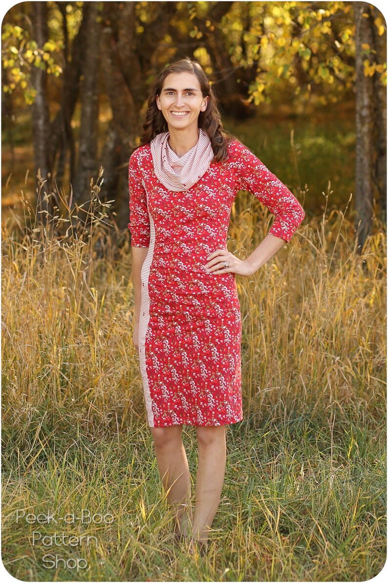 May include: A woman wearing a red floral dress with a white and red striped scarf. The dress has a side panel of white and red stripes. She is standing in a field of tall grass.