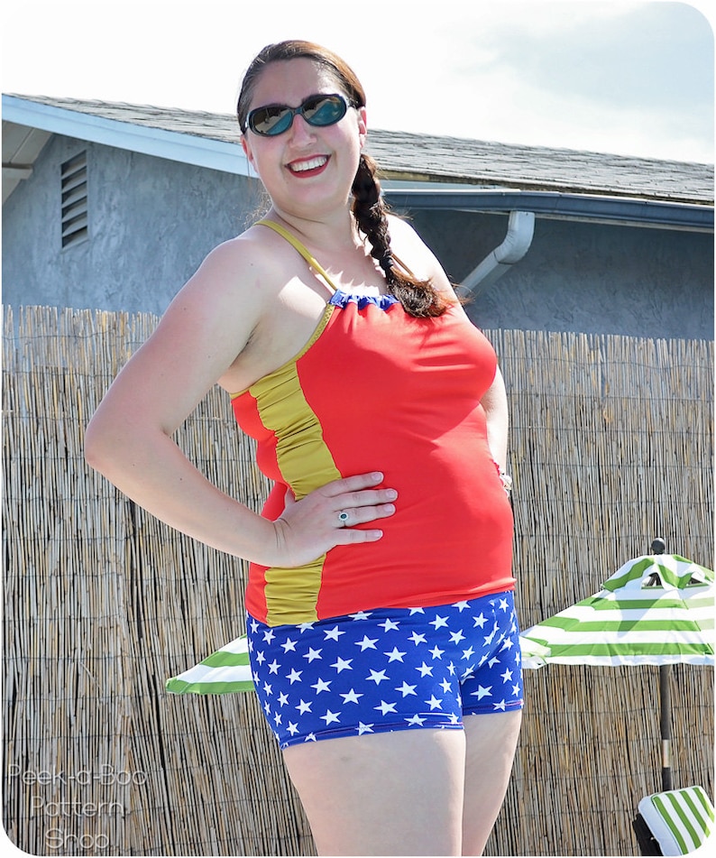 May include: A woman wearing a red and gold swimsuit top with a blue and white star print bottom. She is wearing sunglasses and has her hair in a braid.