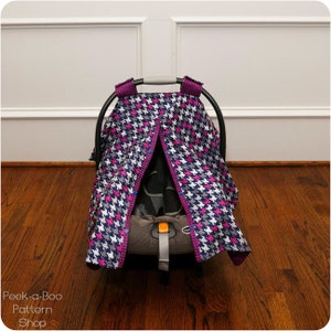 May include: A black and white houndstooth car seat canopy with pink accents. The canopy has a zipper opening in the front and is made of a soft, breathable fabric.