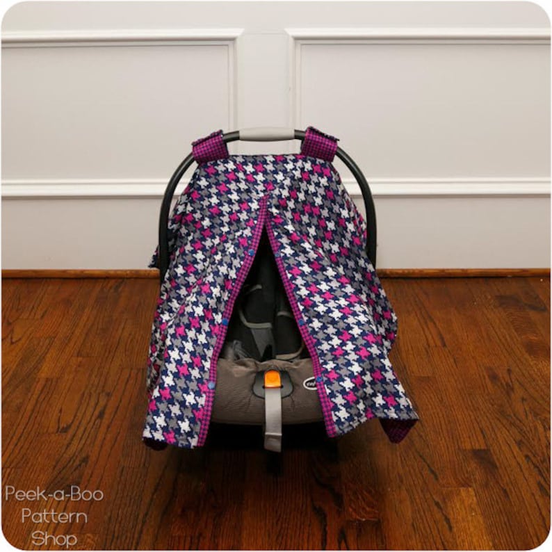 May include: A black and white houndstooth car seat canopy with pink accents. The canopy has a zipper opening in the front and is made of a soft, breathable fabric.