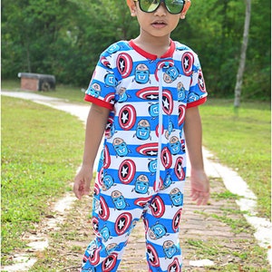 May include: A young child wearing a blue and red jumpsuit with a pattern of Captain America's shield and face. The jumpsuit has a zipper down the front and red cuffs. The child is wearing blue and yellow sunglasses and blue and white shoes.