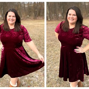 Pode incluir: Uma mulher vestindo um vestido de veludo vinho com mangas curtas e saia rodada. Ela est&aacute; em p&eacute; em uma &aacute;rea gramada com &aacute;rvores ao fundo.