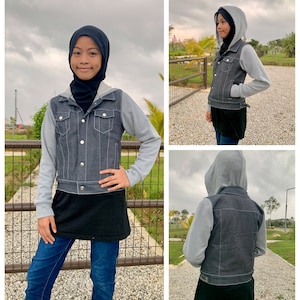 May include: A gray denim jacket with a gray hooded sweatshirt attached. The jacket has silver buttons and pockets. The person is wearing blue jeans and a black top. The background is a park with a fence.