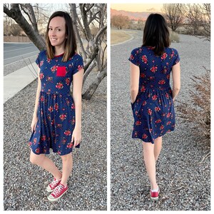 Pode incluir: Um vestido de estampa floral azul e vermelho com mangas curtas e um bolso vermelho na frente. O vestido tem um corpete ajustado e uma saia fluida. A modelo est&aacute; usando t&ecirc;nis vermelhos.