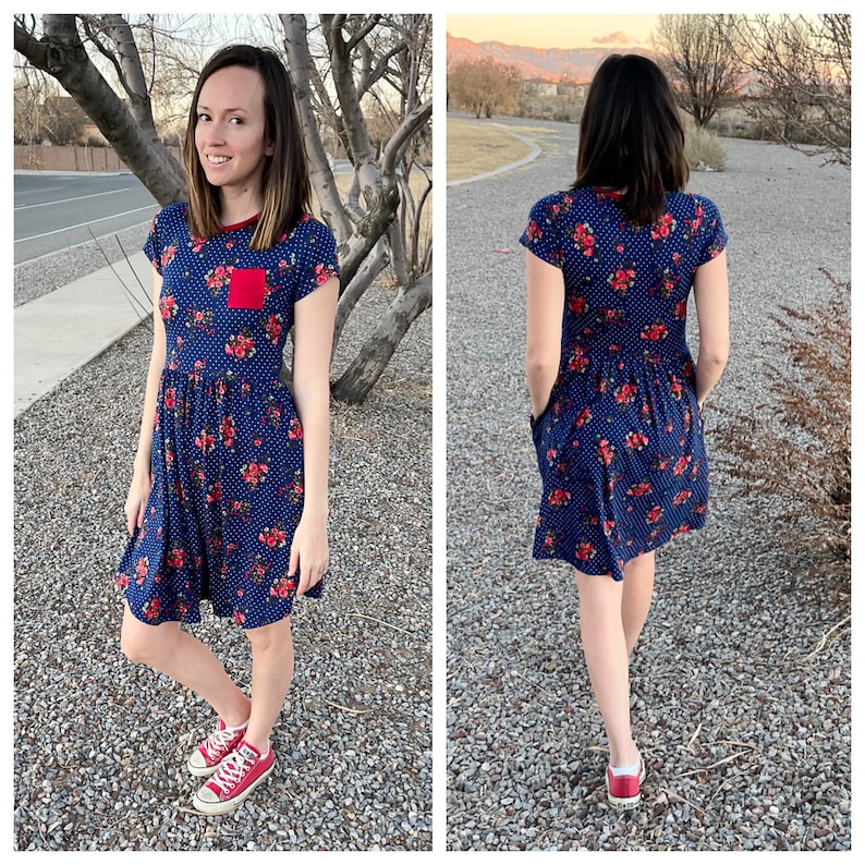 Pode incluir: Um vestido de estampa floral azul e vermelho com mangas curtas e um bolso vermelho na frente. O vestido tem um corpete ajustado e uma saia fluida. A modelo est&aacute; usando t&ecirc;nis vermelhos.