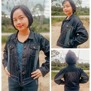May include: A dark blue denim jacket with button closures and pockets. The jacket is worn with a patterned top and matching jeans. The jacket has a classic collar and long sleeves. The denim jacket is a versatile piece of clothing.