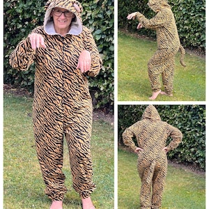 May include: A person wearing a tiger-print onesie with a hood. The onesie has a tail and is brown and black. The person is standing in a grassy area.