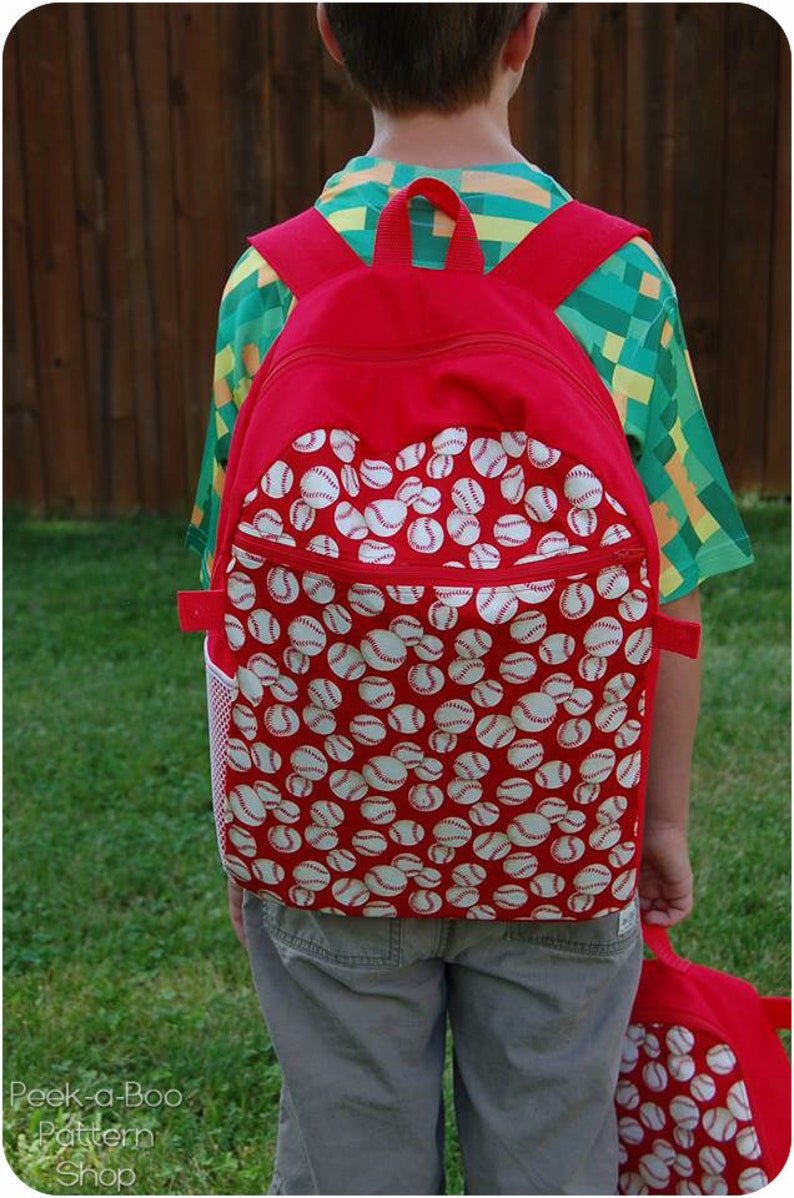 May include: A red backpack with a white baseball pattern. The backpack has a mesh side pocket and a zippered front pocket.